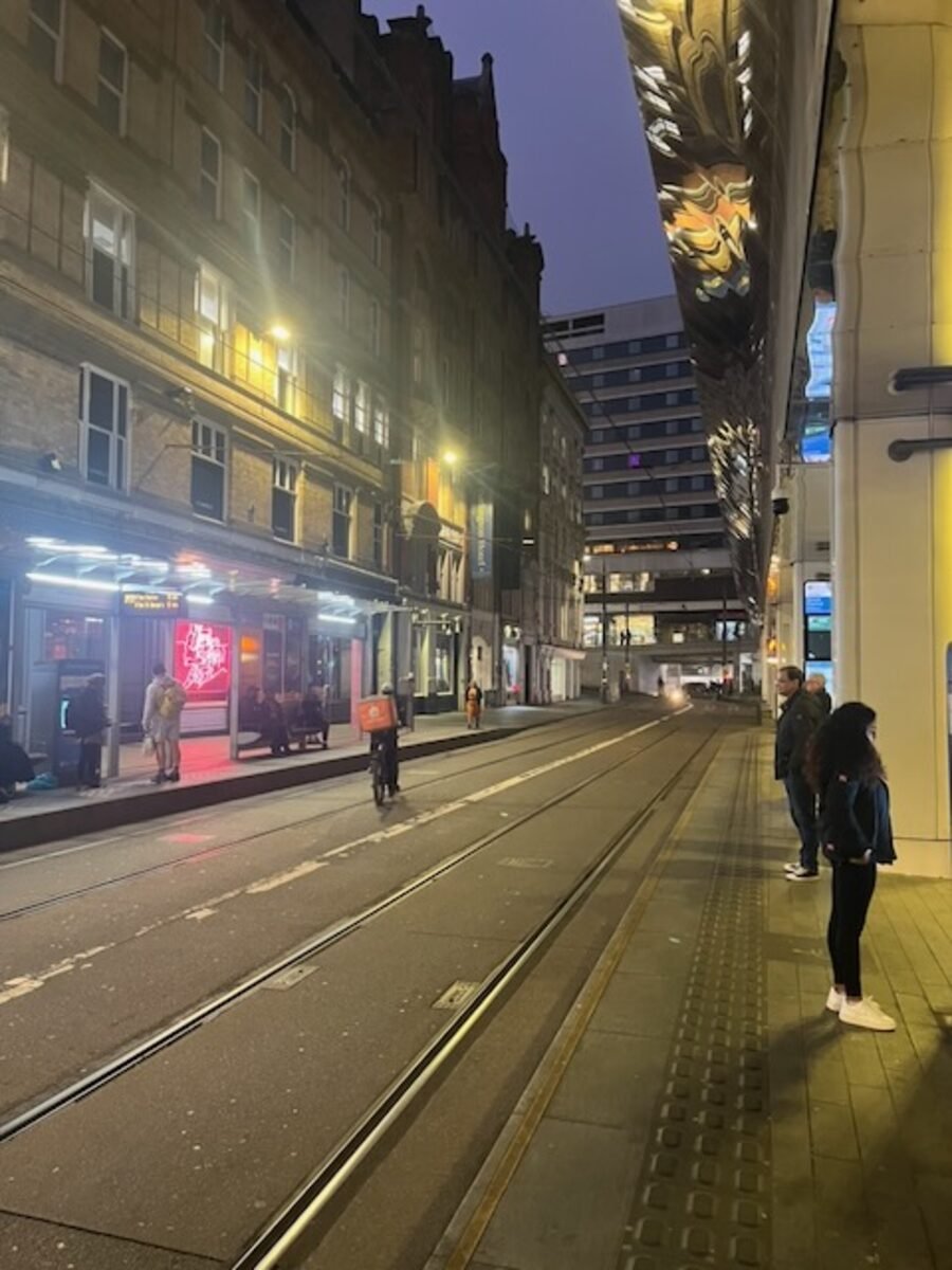 A Birmingham city street at night, tram lines wet under the lights